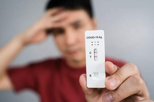 young stressed man holding coronavirus covid 19 positive test result with antigen rapid test kit atk